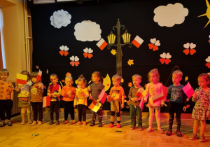 Grupa dzieci z chorągiewkami biorą udział w program artystyczny.