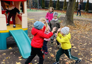 Grupa dzieci bawiących się na placu zabaw wśród jesiennych liści.
