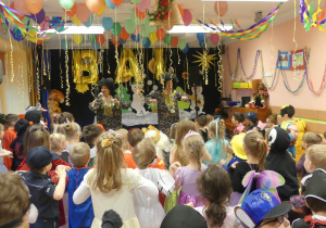 Dzieci w karnawałowych strojach tańczą na udekorowanej sempertyną sali.